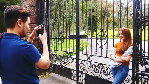 Young woman photographing through camera while standing on railing