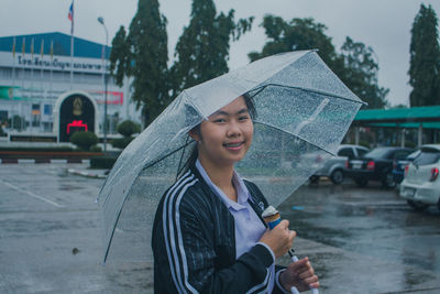 Portrait of smiling young woman holding umbrella while standing in city during rainy season