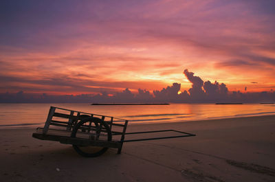 Cart on shore at beach against sky during sunset