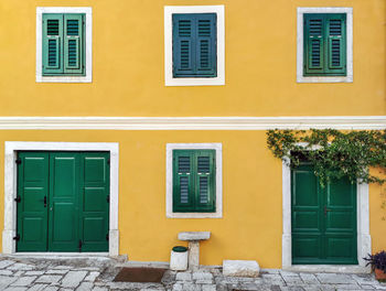 Yellow house with green doors and window shutters.
