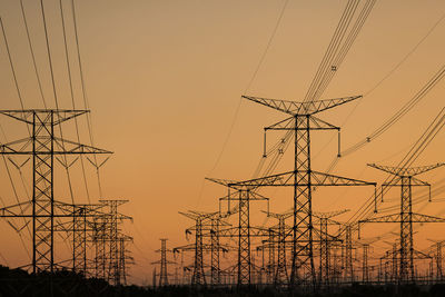 Low angle view of silhouette electricity pylons against orange sky