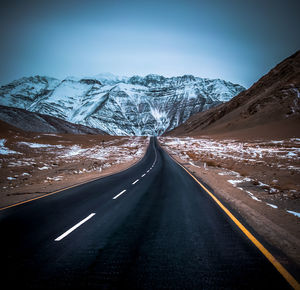 Road amidst snowcapped mountains against sky during winter