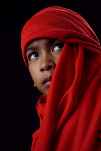 Portrait of teenage girl wearing red hat against black background