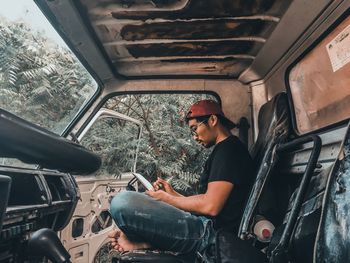 Side view of young man writing on book while sitting in car