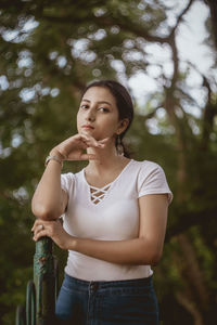 Portrait of beautiful young woman standing against trees