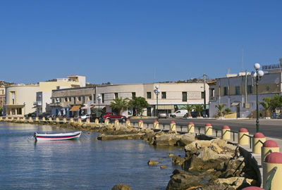 Sailboats in river by buildings against clear blue sky