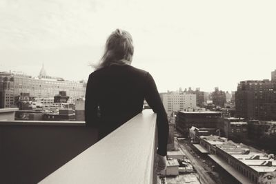 Rear view of man looking at cityscape against clear sky