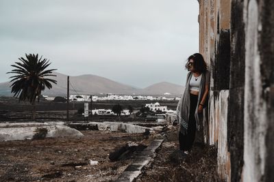 Portrait of young woman standing by tree against sky