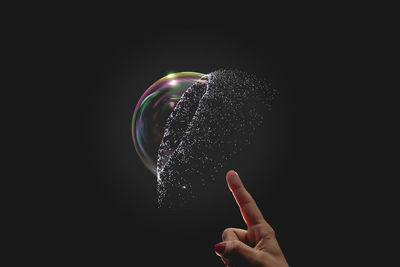 Cropped image of hand bursting a bubble against black backbround