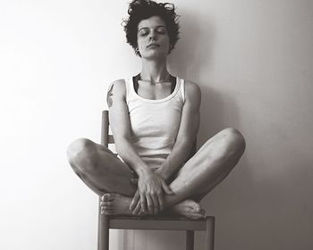 Portrait of young woman sitting on chair against wall