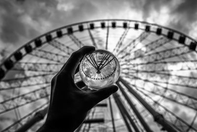 Cropped hand of person holding crystal ball with reflection of ferris wheel