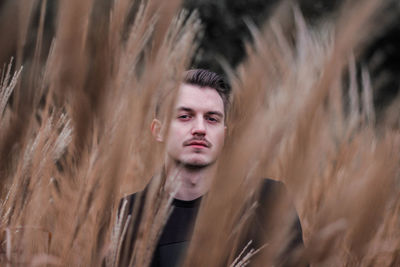 Portrait of young man seen through stalks standing on field