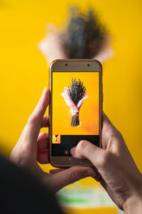 Midsection of person photographing yellow smart phone