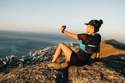 Woman taking selfie while resting on rock
