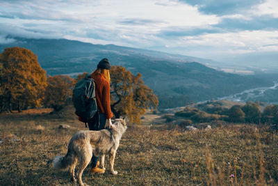 Rear view of woman with dog on mountain against sky