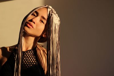 Portrait of young woman wearing wig against wall