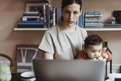 Businesswoman using laptop while sitting with baby boy at home