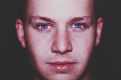 Close-up portrait of young man with purple eyes against black background