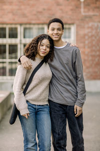 Portrait of smiling male and female teenage student standing with arms around in high school campus