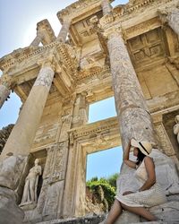 Low angle view of woman sitting in front of historical building