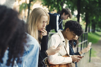 Male and female friends using smart phones in park