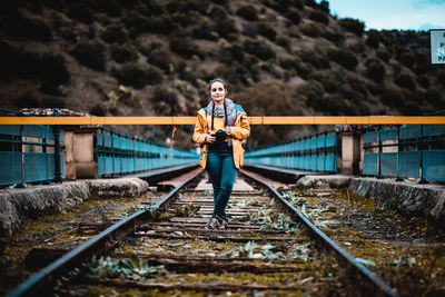 Woman holding camera while standing on railroad track