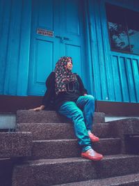 Low angle view of mid adult woman wearing hijab looking away while sitting on steps against built structure