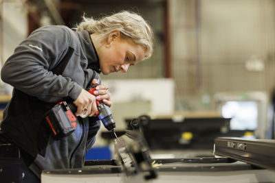 Woman using drilling machine in factory