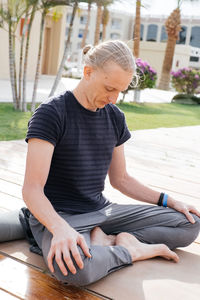 Man practicing yoga on the pier of resort over palm trees. breathing outdoors. inhale fresh air