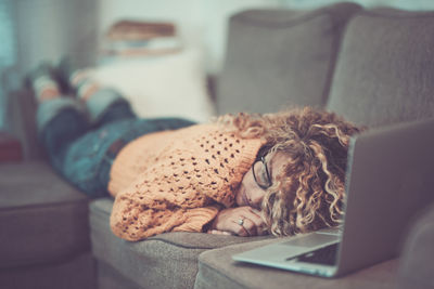 Woman sleeping by laptop on sofa at home