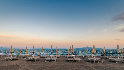 Chairs on beach against sky during sunset