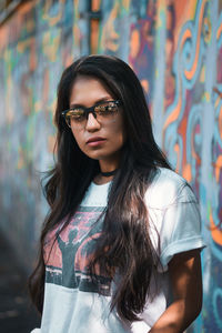 Portrait of young woman wearing sunglasses standing against wall