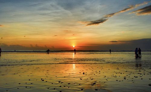 Silhouette people on beach against sky during sunset