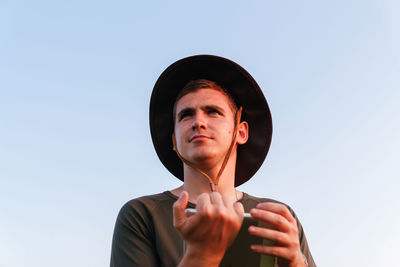 Young man smiling farmer in cowboy hat at agricultural field holding tablet. male on blue sky 