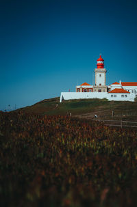 Lighthouse on field against clear blue sky