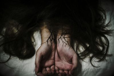 Hair on cropped hands of woman with tattoo at bed