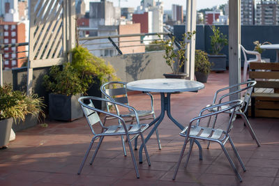 Empty chairs and tables at sidewalk cafe amidst buildings in city