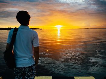 Rear view of man looking at sea against sky during sunset.