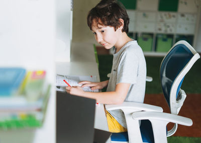 Tween boy do homework learn foreign language writing in pupil book with opened laptop 