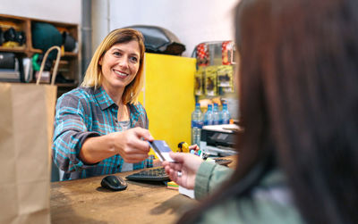 Smiling woman shop assistant taking credit card of client to charge purchase. local commerce concept