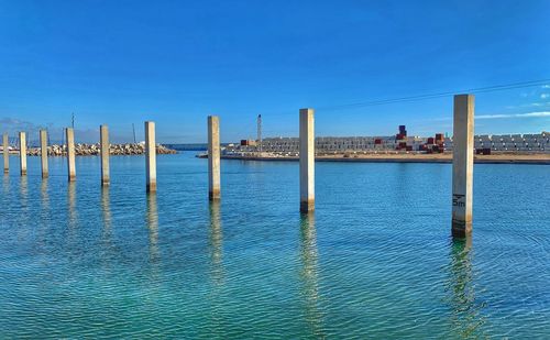 Wooden posts in sea against clear blue sky