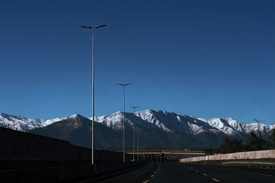 Street amidst snowcapped mountains against clear blue sky