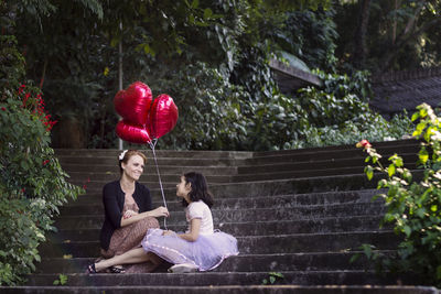 Mother and daughter holding heart shaped balloons while sitting on steps