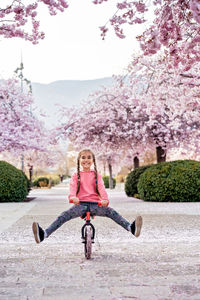 Happy smiling girl riding balance bike with her legs up on bloomimg spring sakura alley