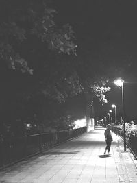 Rear view of man walking on illuminated street at night