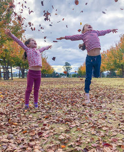 Full length of woman with arms outstretched leaves during autumn