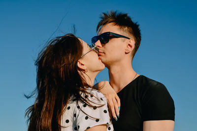 Portrait of young woman wearing sunglasses against blue sky