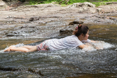 Side view of woman lying on rock in river