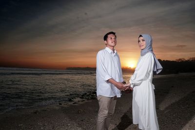 Young couple standing on land against sky during sunset