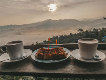 Coffee cup and dessert on table against mountains